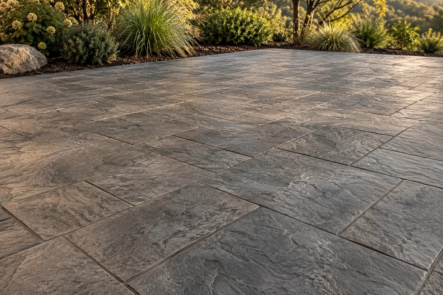 Illustrative smoke-gray stamped concrete patio with an ashlar slate pattern and a planted border